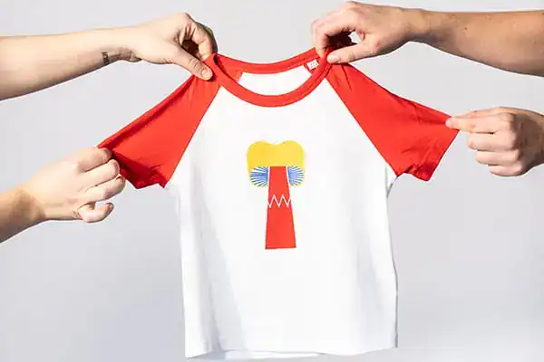 Two hands hold up a white t-shirt with red raglan sleeves and a tooth and toothbrush graphic design.