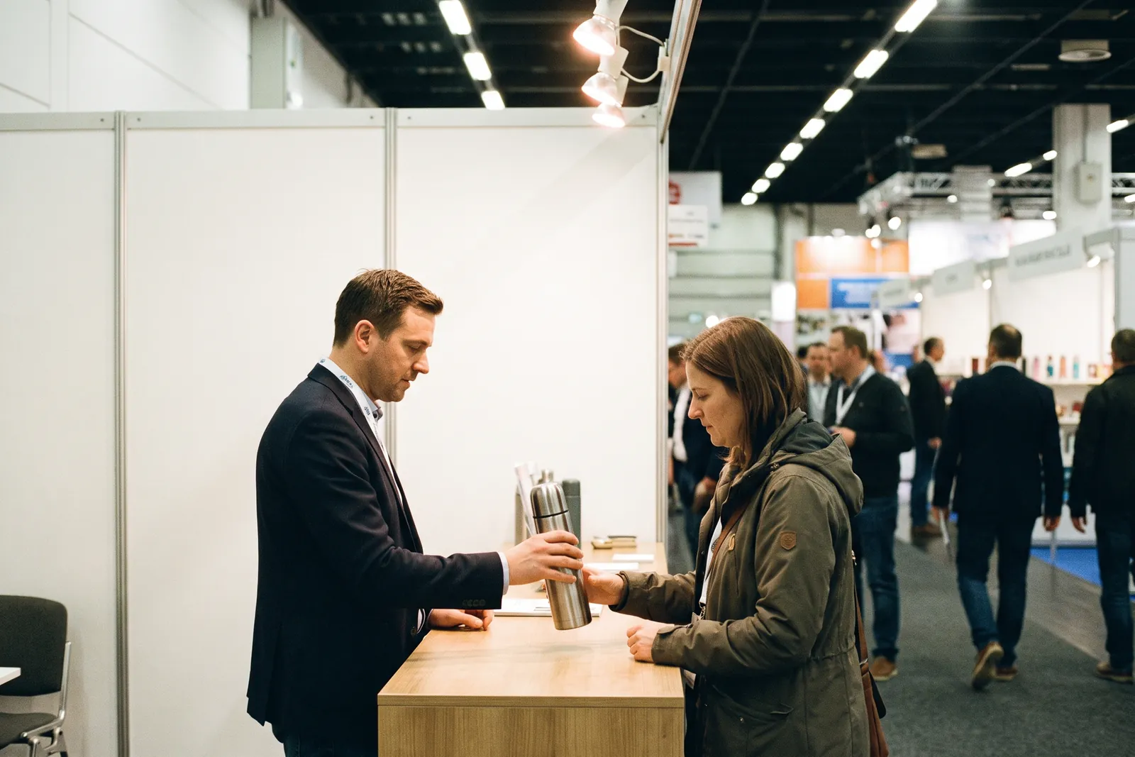 Stand staff handing a vacuum flask to a visitor after a conversation at a trade fair